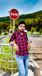 An indian  young man standing at the traffic post in front of stop signal. 