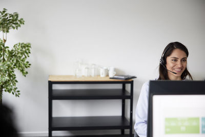 Smiling mid adult businesswoman using headset in office in front of computer screen