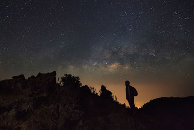 Silhouette people standing on rock against sky at night