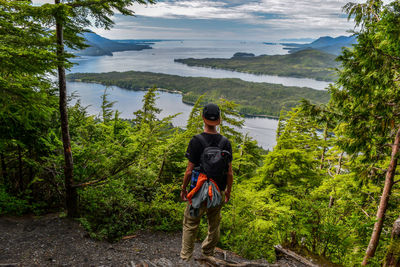 Rear view of man with backpack standing against lake