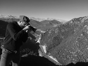 Man photographing while standing on mountain against clear sky