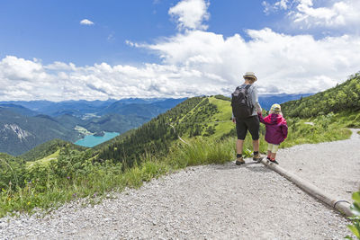 Mother and daughter hiking on mountain road against sky