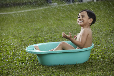 Happy boy sitting in bathtub on grass at back yard