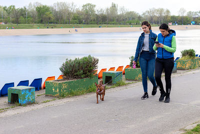 Mother and her teen girl walking with pinscher dog by the of relationship between human and animal.