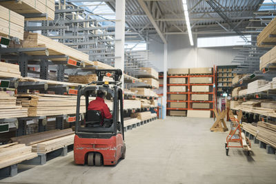 Rear view of salesman driving forklift in warehouse at hardware store