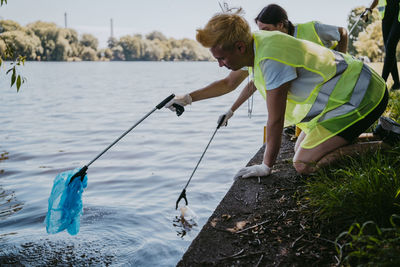 Male and female environmentalists picking up plastics with claws from lake
