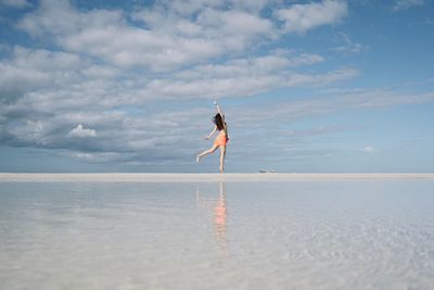 Woman flying over beach against sky