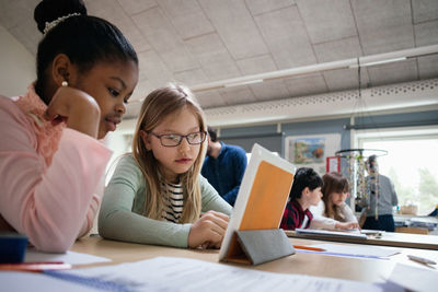 Female students reading digital tablet at desk in classroom