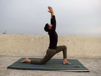 Full length of man with arms raised exercising against sky