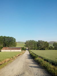 Empty road in field against clear blue sky