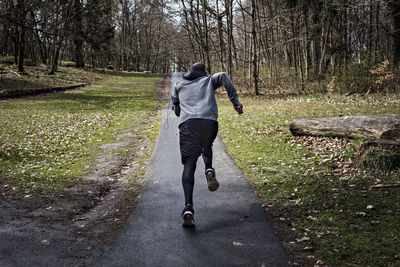 Full length rear view of determined male athlete jogging on narrow street in forest