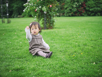 Cute baby girl sitting on grassy field at park