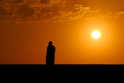 Silhouette man standing against orange sky during sunset