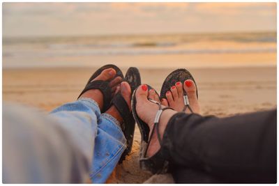 Low section of couple sitting on sand at beach