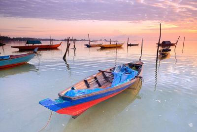 Boats moored in sea against sky during sunset