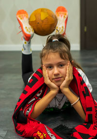 The girl is lying on the floor with a fan scarf and a ball at her feet.