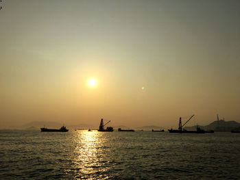 Silhouette boats in sea against sky during sunset