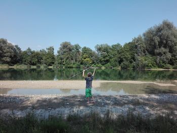 Boy standing by lake against sky