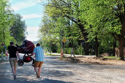 Rear view of people walking on road against trees