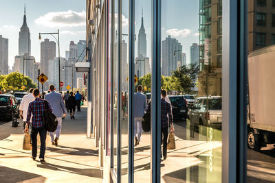 Rear view of people walking on footpath by building