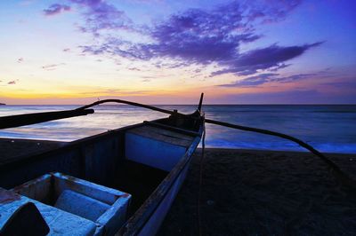 Outrigger boat moored on shore at beach against sky during sunset
