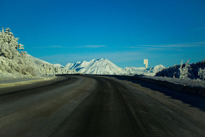 Empty road by mountain against blue sky