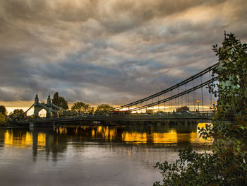 Hammersmith bridge over river against cloudy sky