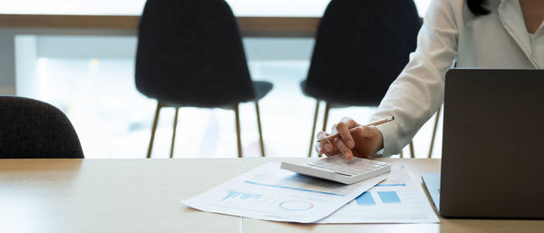 Midsection of woman using smart phone while sitting on table