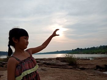 Girl standing by lake during sunset