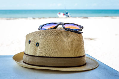 Close-up of hat and sunglasses on table against sea at beach