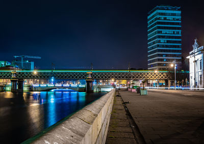 Illuminated bridge over river against buildings at night