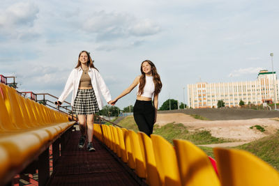 Two teenage girls walk together through the stands of the school stadium, talking, holding hands, 