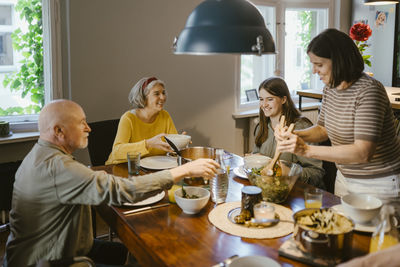 Smiling woman serving salad to family while having dinner on dining table at home