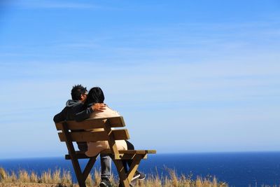 Rear view of couple sitting on bench against sea