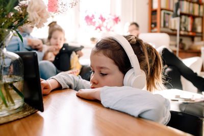 Girl listening music through headphones and using digital tablet with family in background