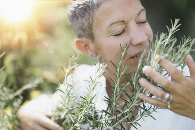 Woman with eyes closed holding while smelling rosemary plant