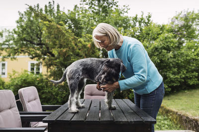 Senior woman cutting dog's nails on table at yard