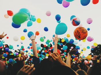 Crowd throwing colorful balloons against sky during festival