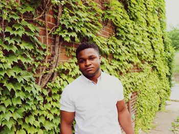 Portrait of young man standing by ivies