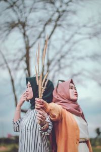 Midsection of woman holding plant against trees