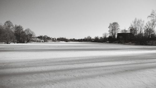 Trees on snow covered field against clear sky