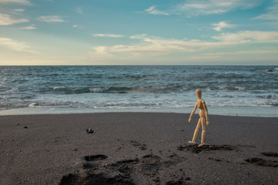 A wooden dummy walks along the beach with black sand