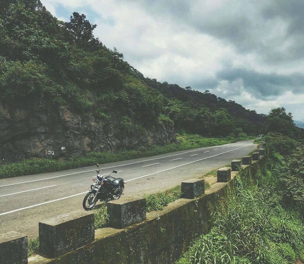 MAN RIDING MOTORCYCLE ON ROAD AGAINST MOUNTAIN