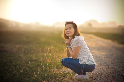 Portrait of woman crouching on field against sky during sunset