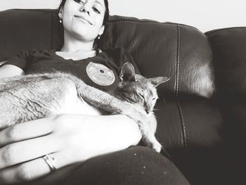 Low angle portrait of mid adult woman with cat sitting on sofa at home