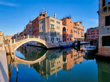 Reflection of buildings on water in canal against blue sky