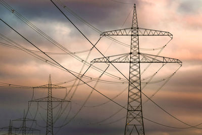 Low angle view of electricity pylon against sky at sunset