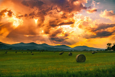 Hay bales on field against sky during sunset