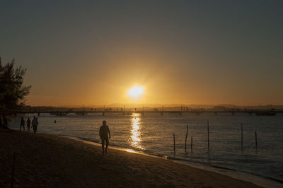 Silhouette people on beach against sky during sunset