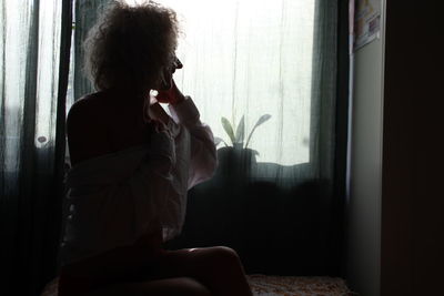 Young woman looking through window at home